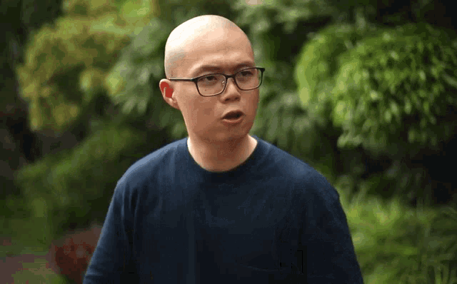 a bald man wearing glasses and a blue sweater looks surprised