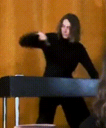 a man in a black turtleneck is standing in front of a piano