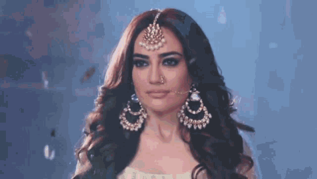 a woman wearing a nose ring , earrings , and a maang tikka .