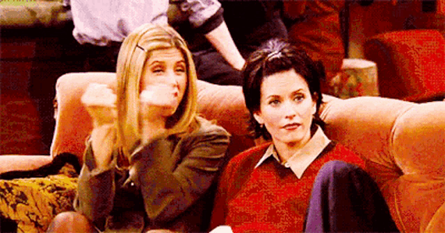 two women are sitting on a couch with their hands in their mouths .
