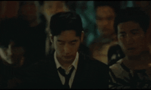a man in a suit and tie is standing in a crowd of people in a dark room .