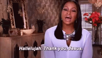 a woman in a white shirt is standing in a living room and saying `` hallelujah , thank you , jesus . ''