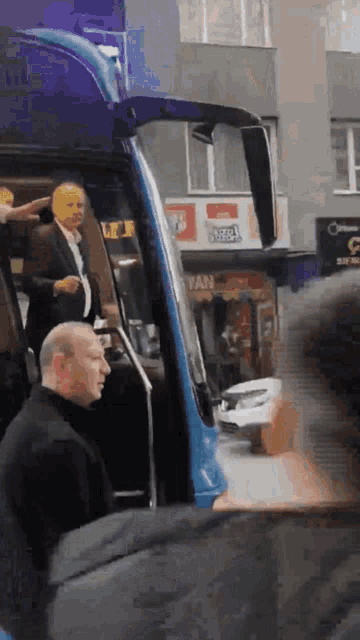 a man in a suit is getting out of a blue bus in front of a sign that says fan