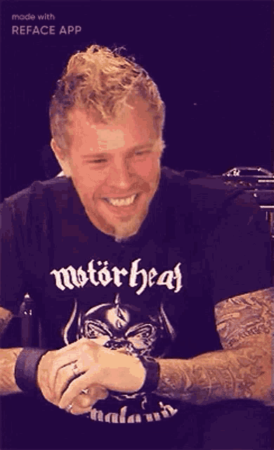 a man wearing a motorhead t-shirt is smiling while sitting down .