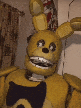 a yellow stuffed animal with a black bow tie is sitting on a bed