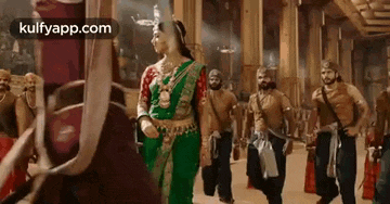 a woman in a green sari is standing next to a group of men in a room .