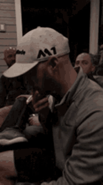 a man wearing a hat with the letter m on it is smoking a cigarette