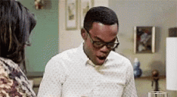 a man wearing glasses is standing in front of a woman in a kitchen with his mouth open .