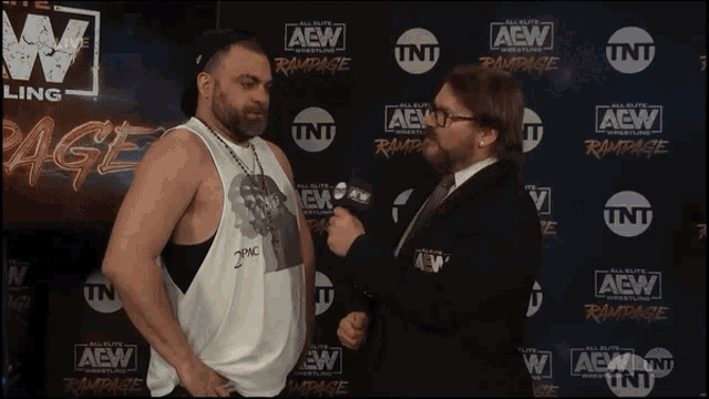 a man talking to another man in front of a wall that says aew
