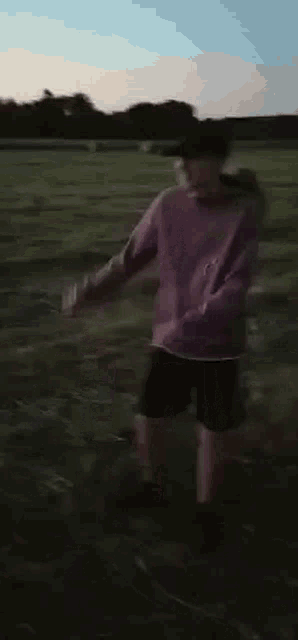a person in a purple sweater and black shorts is standing in a field .