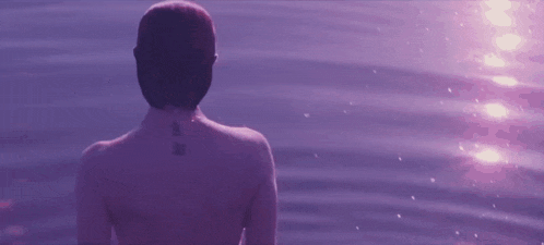 a woman with a tattoo on her back is standing in front of a purple water surface .