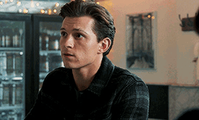a young man in a plaid shirt is sitting at a table in a room .