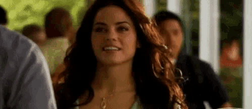 a woman with long hair is smiling and looking at the camera while standing in front of a crowd of people .