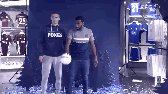 a man wearing a foxes shirt stands next to another man holding a soccer ball