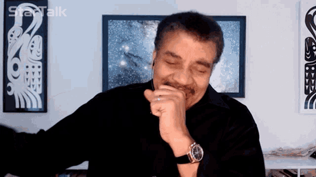 a man wearing a black shirt and a watch stands in front of a framed picture that says ' startalk ' on it