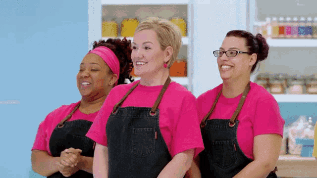 three women wearing pink shirts and black aprons are standing next to each other