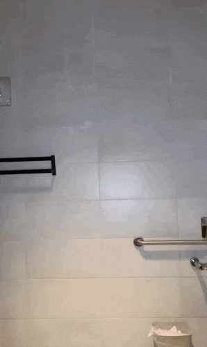 a person standing in a bathroom with a towel rack and a trash can