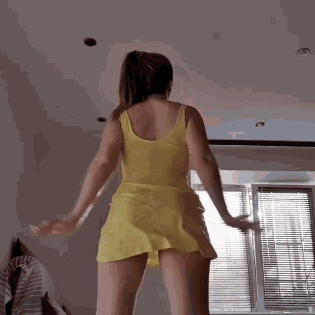 a woman in a yellow dress is standing in front of a window