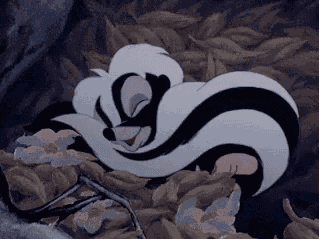 a black and white cartoon skunk is sleeping in a pile of leaves .