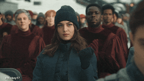 a woman wearing a beanie stands in front of a crowd of people with the hashtag #mickey17 on the bottom