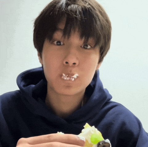 a young man in a blue hoodie is eating a piece of cake with whipped cream on his face