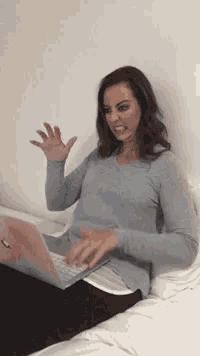a woman is sitting on a bed using a laptop and making a face