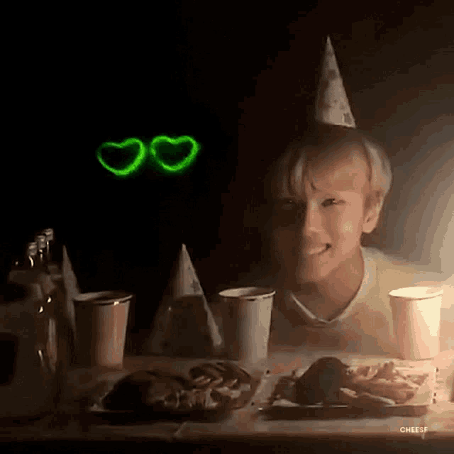 a boy wearing a party hat is sitting at a table with a plate of food and a candle .