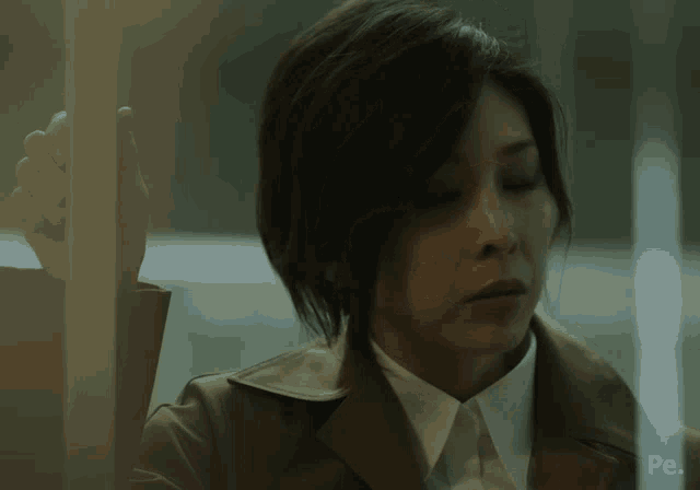 a woman in a trench coat is standing in front of a glass door with the word pe on it