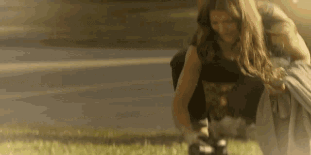 a woman is kneeling down in the grass holding a camera and smiling .