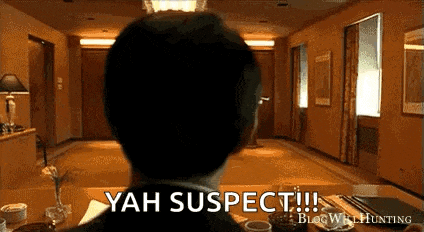a man in a suit is sitting at a table in a room with the words yah suspect written on it .