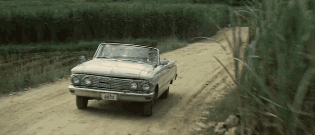 a white convertible car with a license plate that says 6675 is driving down a dirt road