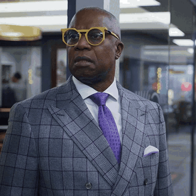 a man wearing glasses and a plaid suit is standing in a hallway