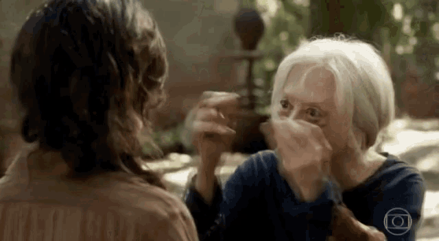a woman with gray hair is covering her face with her hands while talking to another woman .