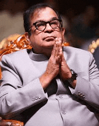 a man wearing glasses is sitting in a chair with his hands folded in prayer .