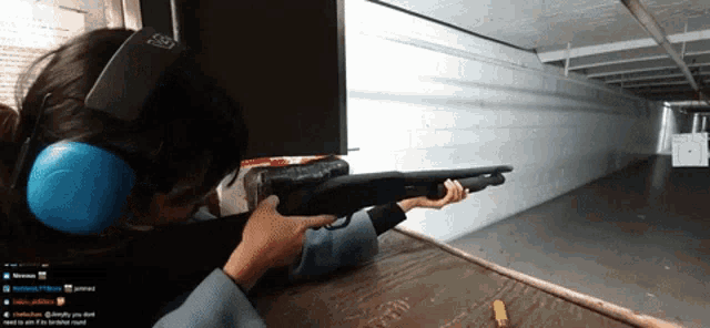 a woman wearing ear protectors is holding a shotgun in a shooting range