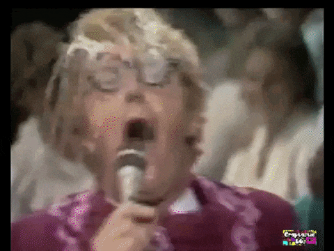 a woman with glasses is singing into a microphone with her mouth wide open .