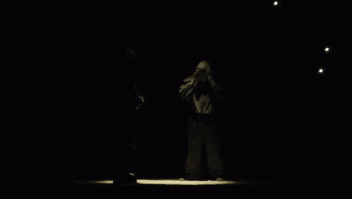 a man in a mask stands in the dark with his hands folded