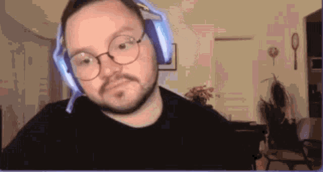 a man with a beard and glasses is wearing headphones and looking at the camera .