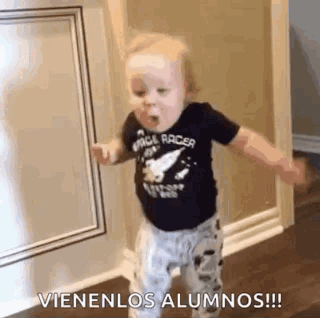 a baby is dancing in a hallway with the words vienenlos alumnos written on the wall behind him .