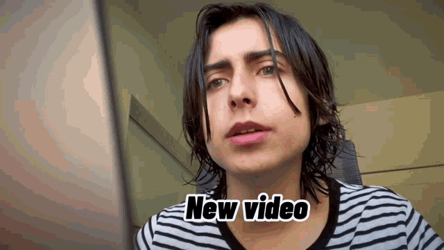 a young man in a striped shirt is looking at a laptop screen with the words " new video " next to him