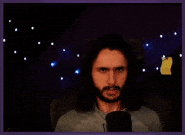 a man with long hair and a beard is sitting in front of a microphone .
