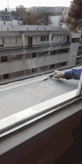 a person is holding a pen in front of a window with a building in the background