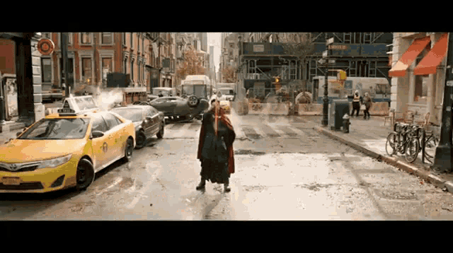 a man in a red cloak stands in the middle of a busy street with a taxi that says nyc on it
