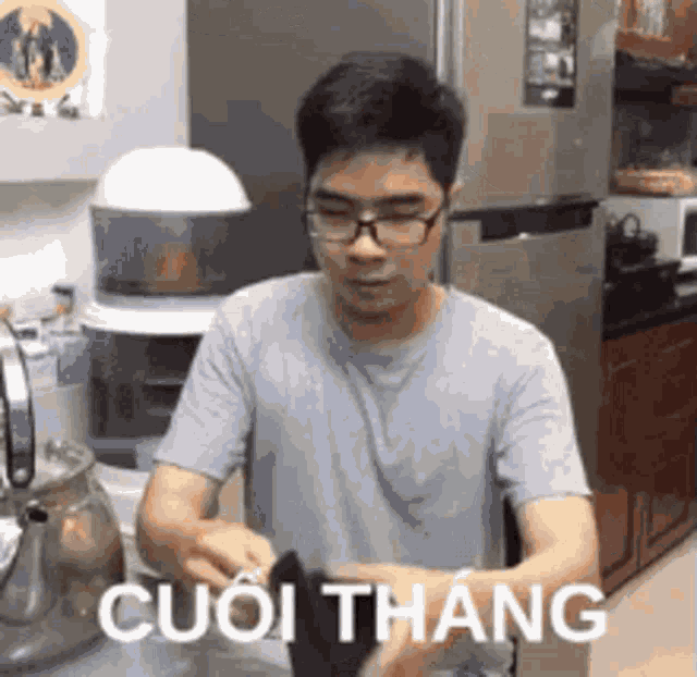 a man wearing glasses is standing in a kitchen with a foreign language on his shirt .