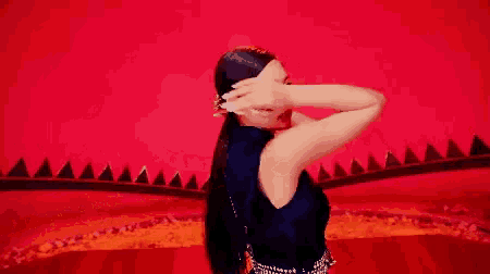 a woman in a black dress with long hair is standing in front of a red background .