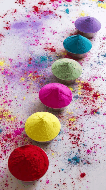 a row of bowls of different colored powders on a white surface