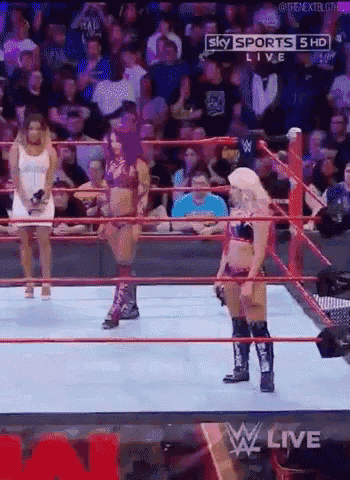 a woman is standing in a wrestling ring while another woman stands behind her .