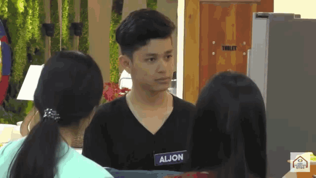 a man with a name tag that says aljon is talking to two women