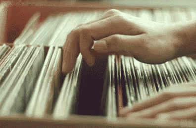 a close up of a person 's hand reaching for a record in a shelf .