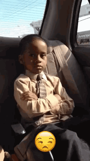a young boy in a suit and tie is sitting in the back seat of a car with his arms crossed